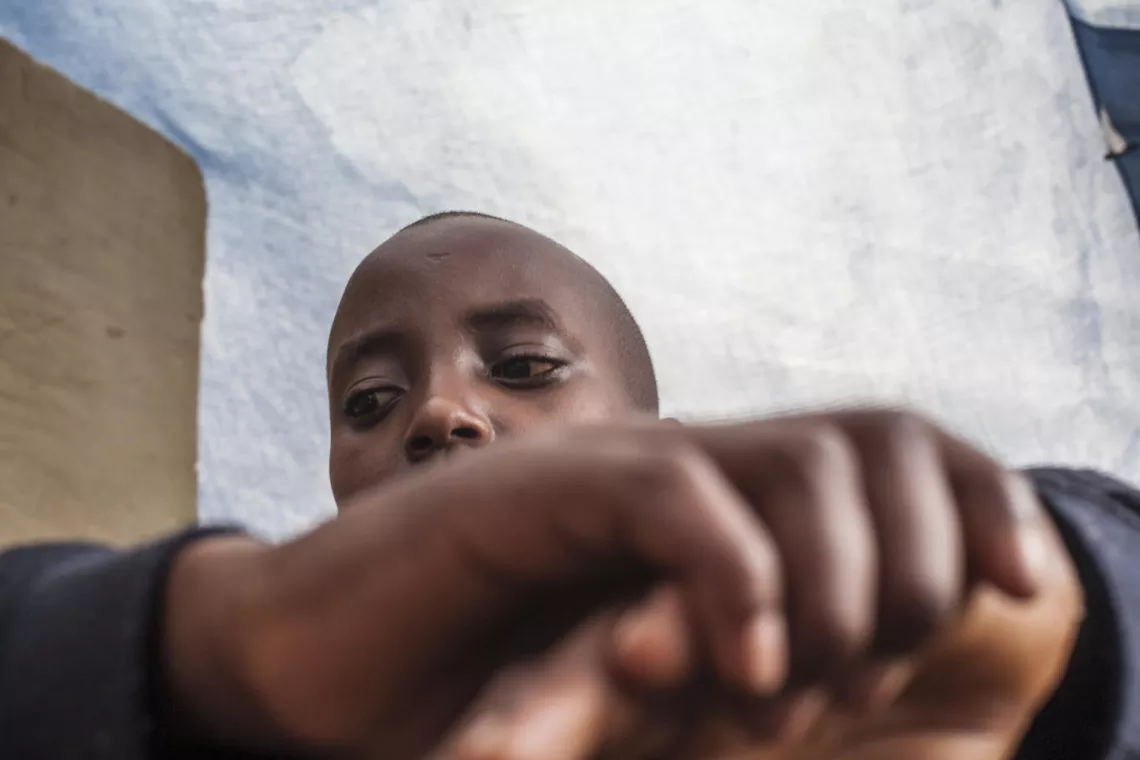 Burundian refugee boy in Rwanda hides his face from camera in camp