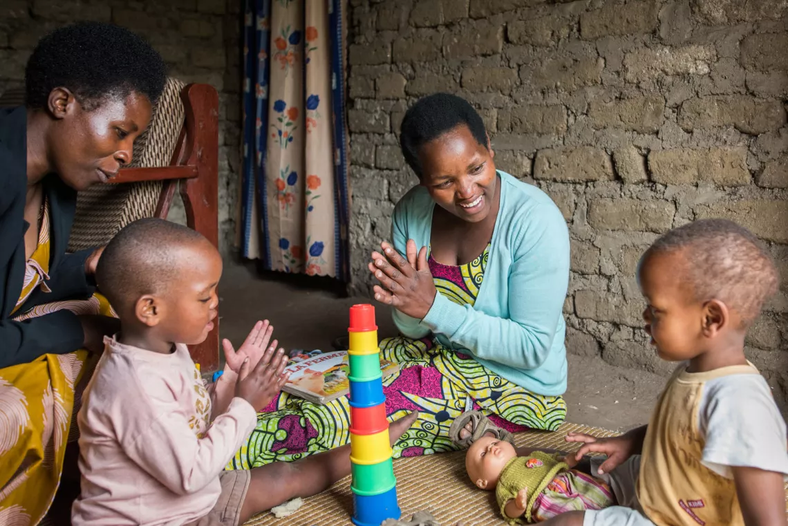 A mother and a trained early childhood caregiver play with children in their home. 