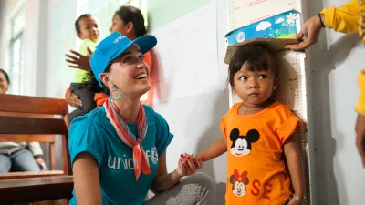 Artist Katy Perry wearing a UNICEF t-shirt and cap holding a small girls hand as she is weighed