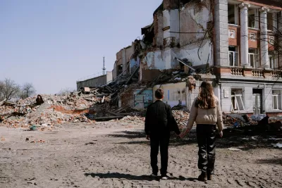 Ukraine. A boy and girl hold hands as they look at a badly damaged building.