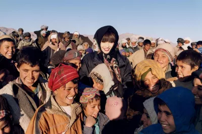 On 6 February, a crowd of other adults behind her, UNICEF Goodwill Ambassador Tetsuko Kuroyanagi (centre) stands amidst a group of smiling children in the late afternoon sun at the Maslakh camp for more than 140,000 displaced persons, set up amidst the ruins of an abandoned village near the western city of Herat, capital of the province of the same name. 