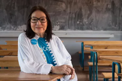 In 2015, UNICEF Goodwill Ambassador Nana Mouskouri, seated at a student’s desk in a classroom, smiles during her visit to a public primary school in Ampangabe Village in Analamanga Region, Madagascar.