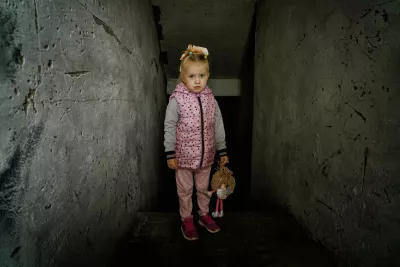 Ukraine. A young girl stands holding a toy in the boiler room of her school.