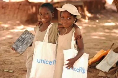 Girls walk arm-in-arm outside Likoli, a UNICEF-supported primary school in the village of Zakpota, in central Benin. UNICEF provides Likoli and surrounding schools with supplies, classroom furniture, and training for teachers. One girl carries a UNICEF-supplied slate. Their book bags bear the UNICEF logo.