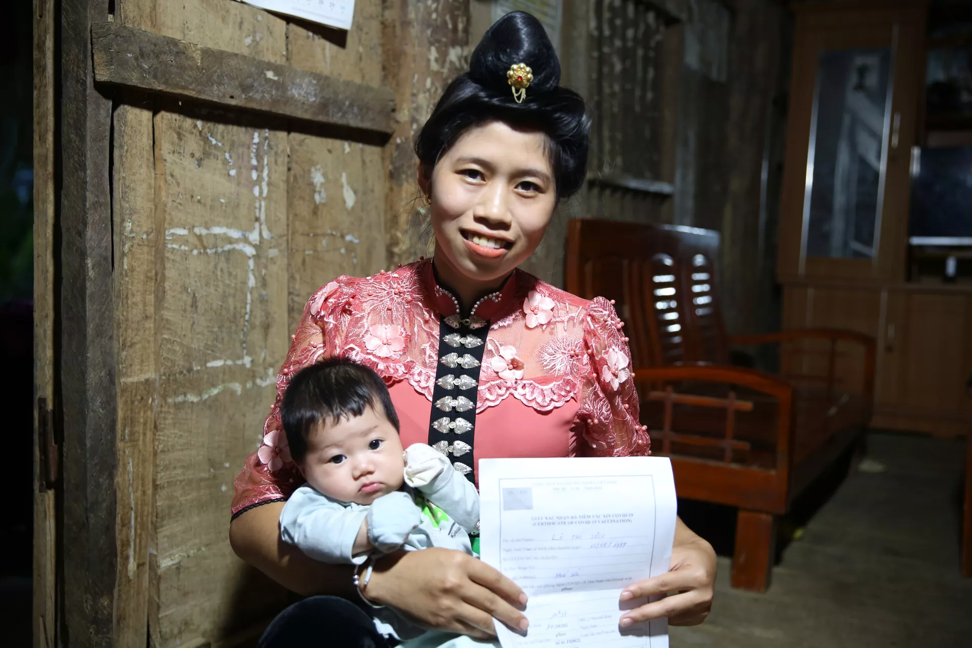 Lo Thi Son holds her daughter and her COVID-19 vaccine certificate