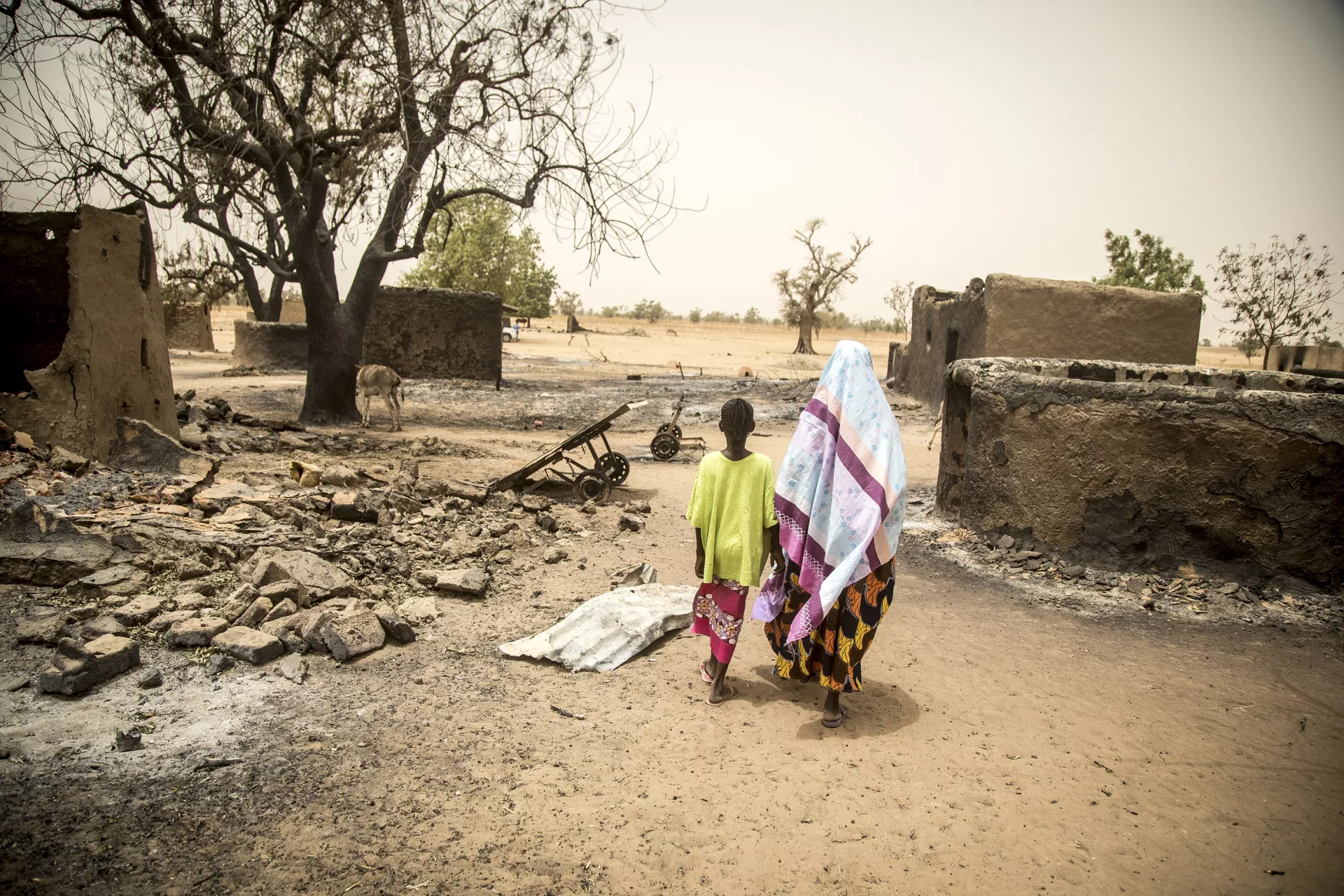 Mali. A woman walks through the remains of a village holding a child's hand.
