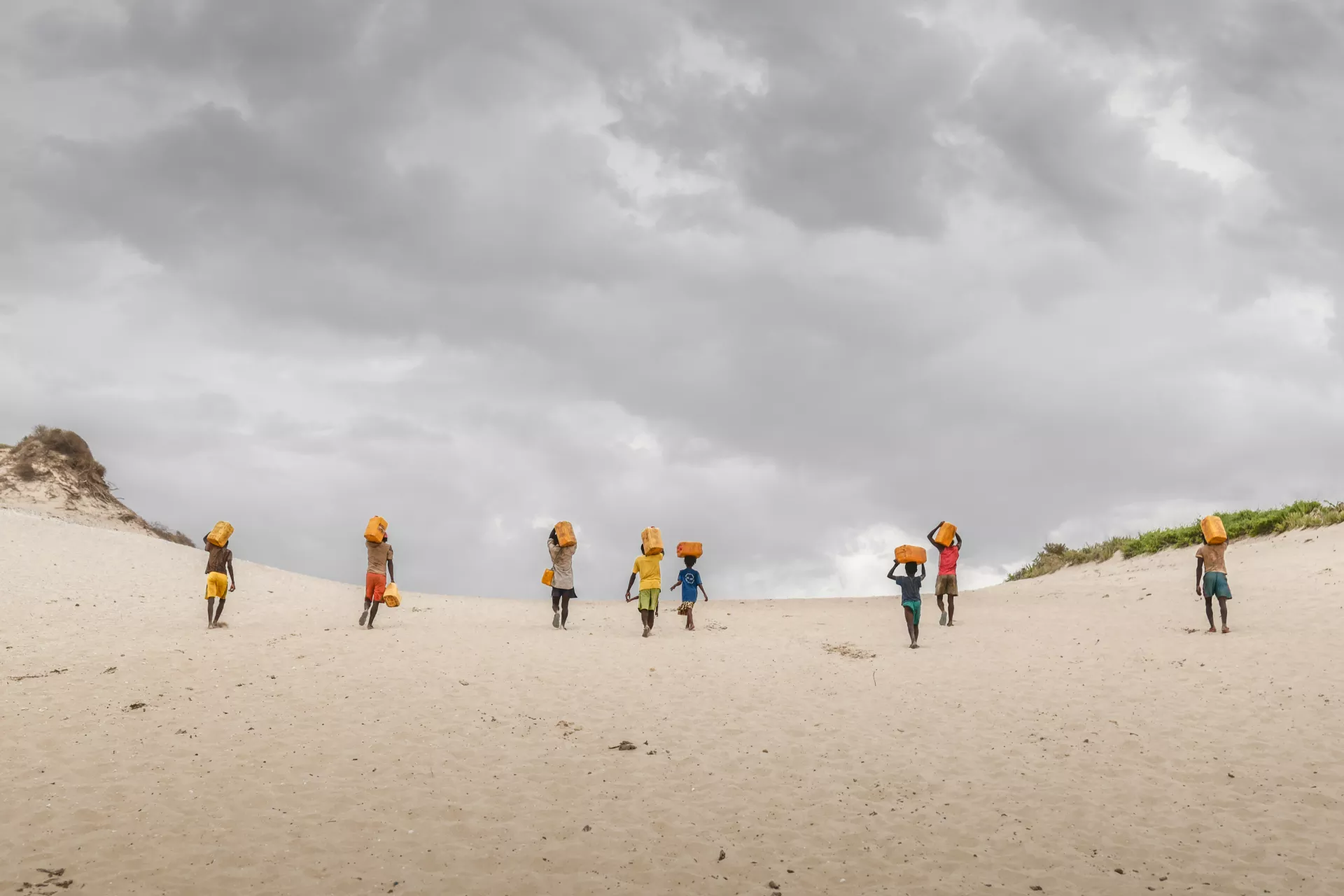 Children walk on sand carrying water
