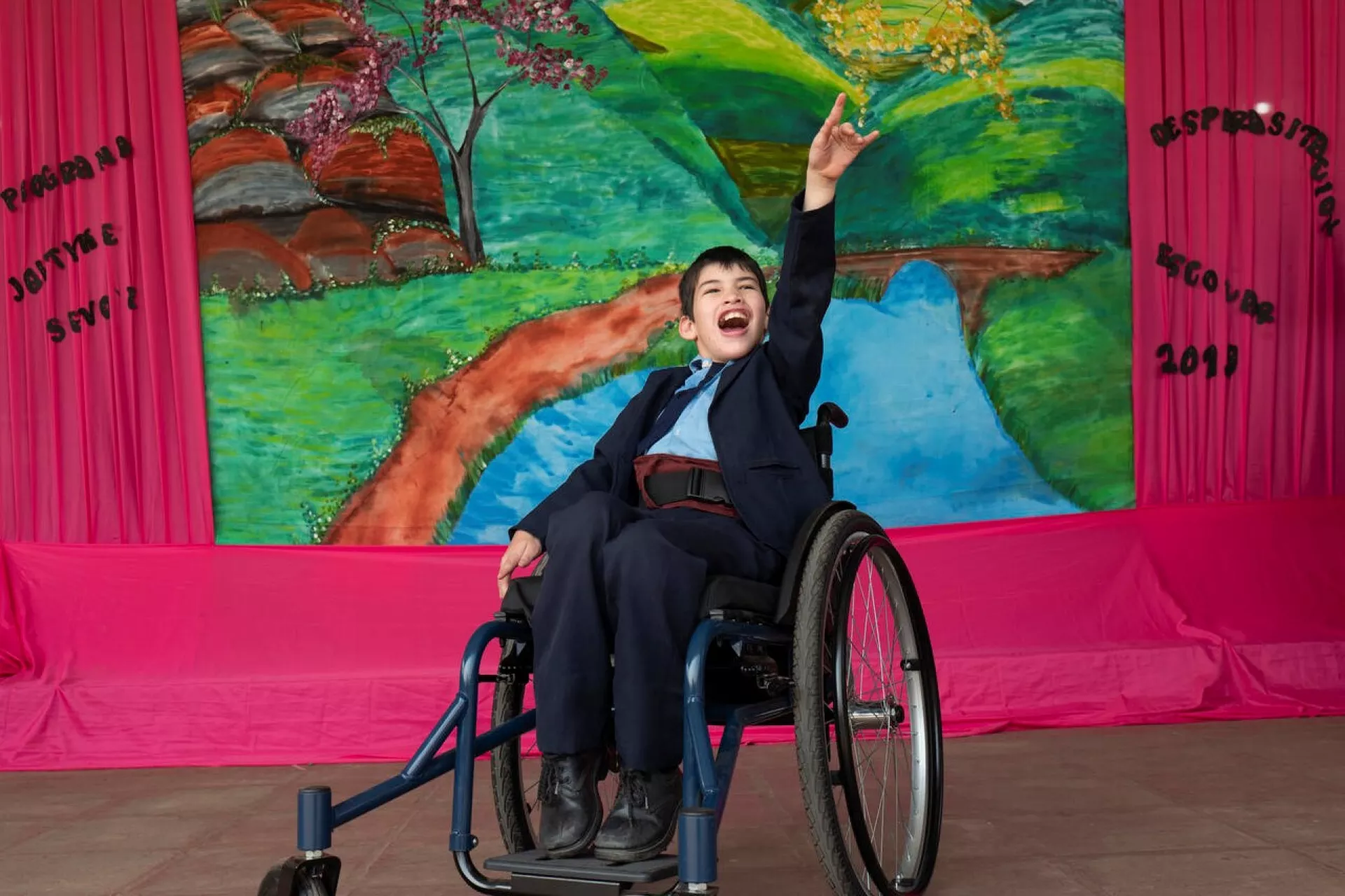 An eleven-year-old boy using a wheelchair shows off his dance moves on a colourful stage. 