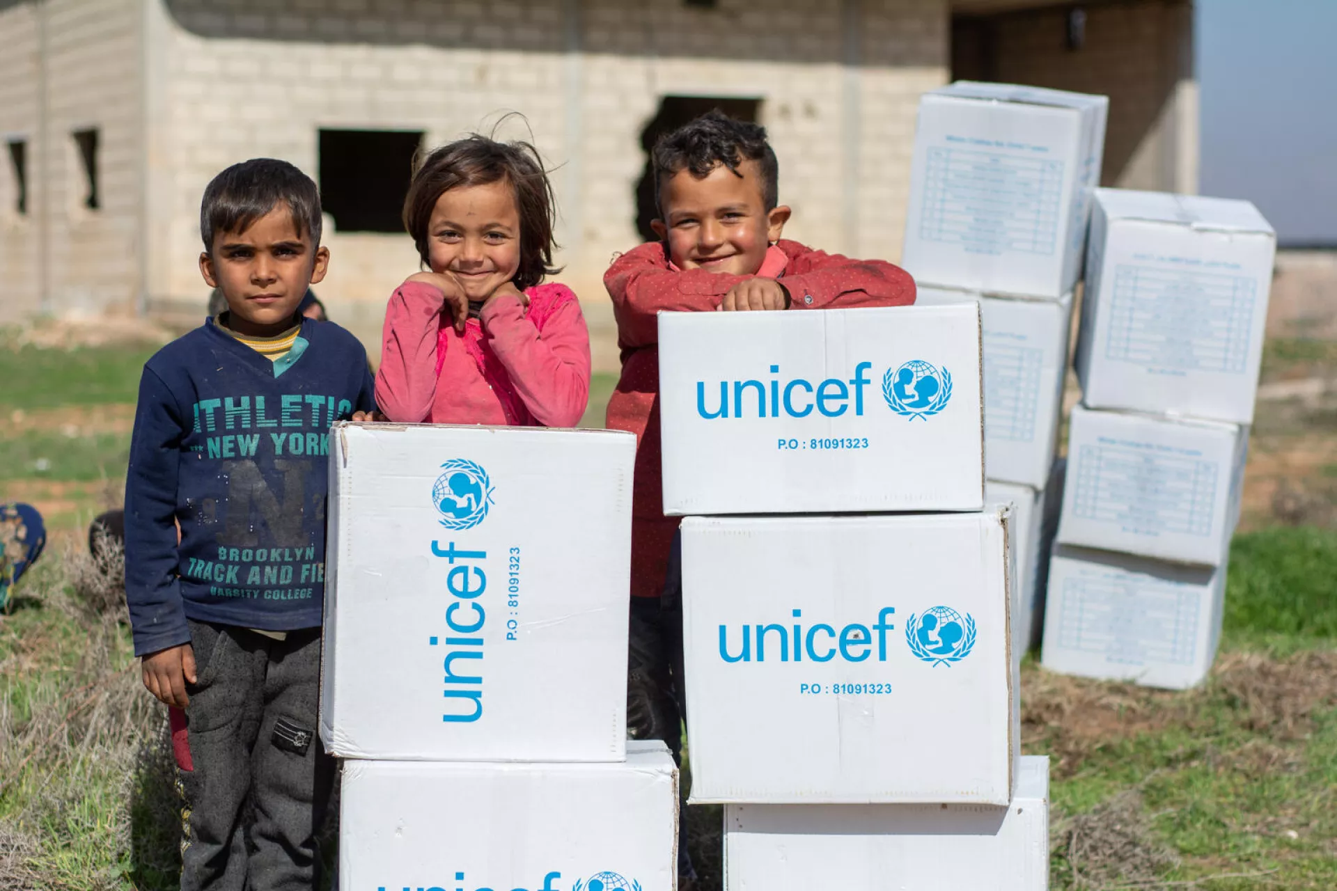 Syria. A groups of children stand behind boxes of supplies.