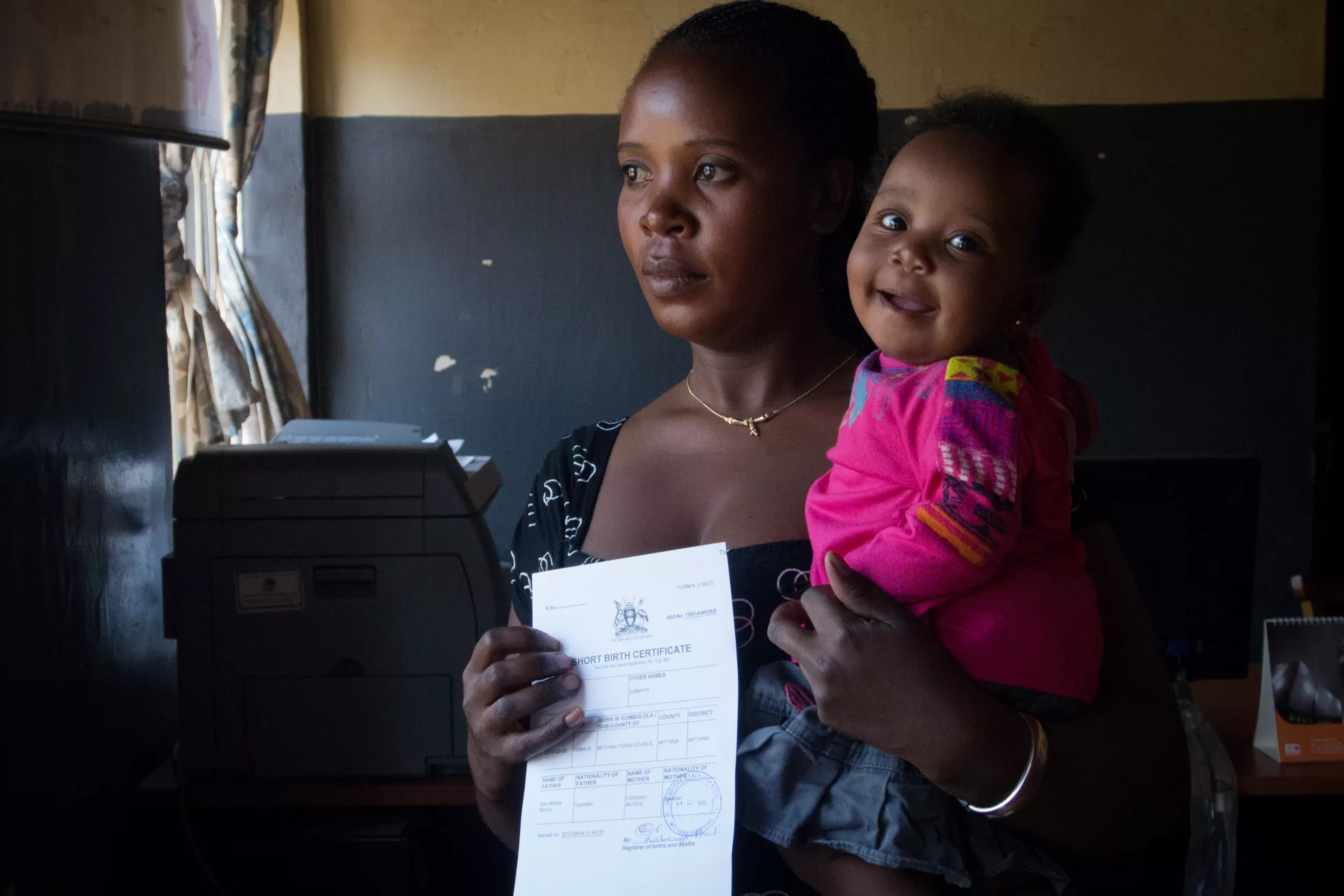 A mother displays her child's birth certificate while holding her child in a hospital in Uganda.