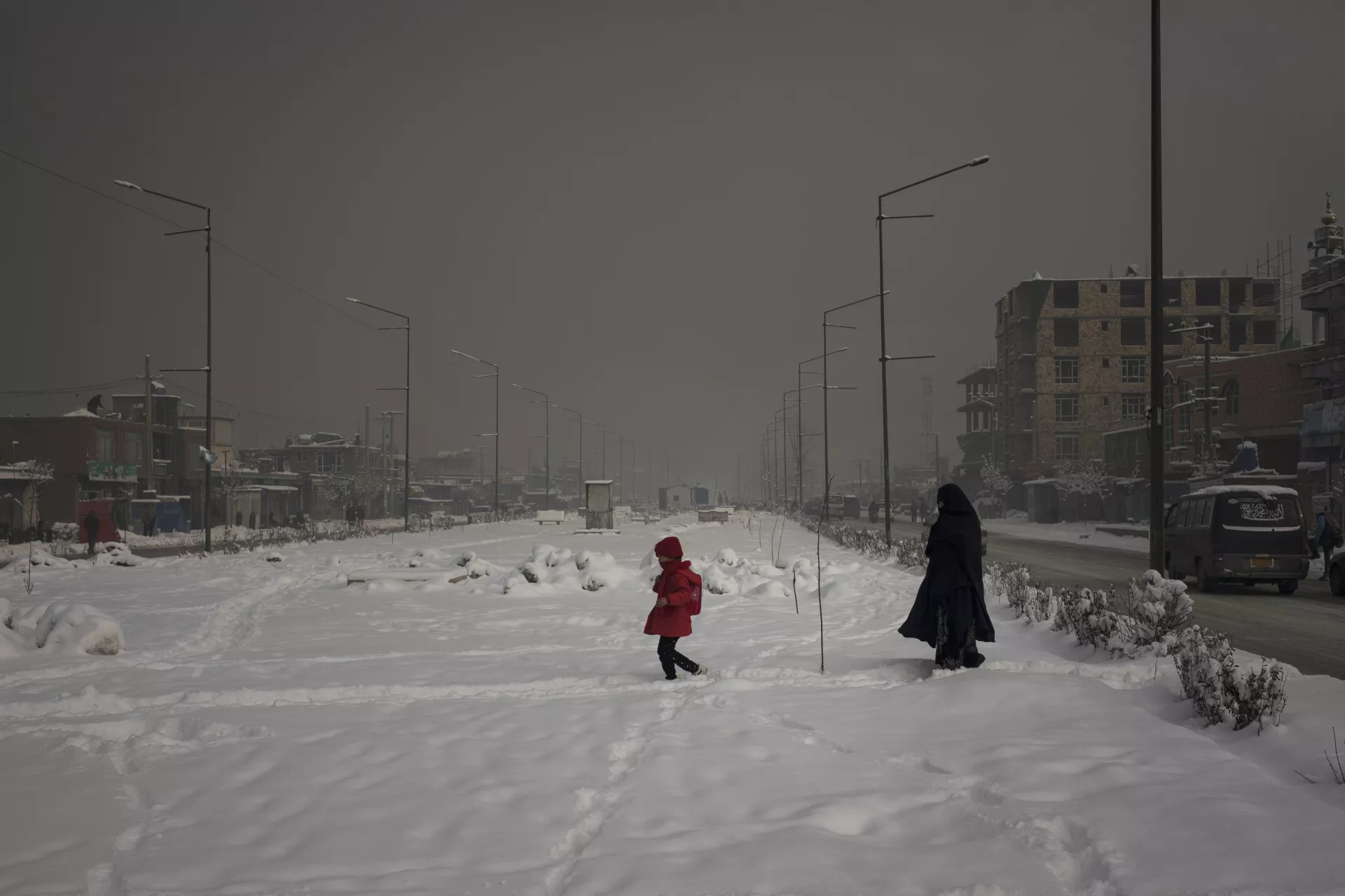 A mother with her daughter walk across a snow covered area of the city during a heavily polluted morning in Kabul, Afghanistan