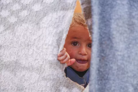 On 16 November 2019 in Idlib governate, Syrian Arab Republic, a child peeks out of a temporary shelter in an informal settlement in Killi, near the border with Turkey.