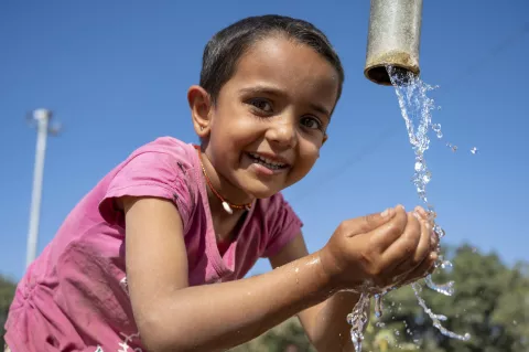 A small girl drinking water from a fountain