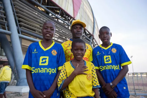 Abordar el registro de nacimientos en Angola: un padre y sus tres hijos están fuera de un estadio de fútbol.