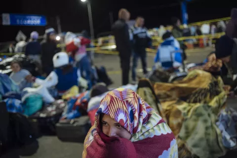 A young Venezuelan woman sits fully covered in a blanket, waiting to continue her journey at Rumichaca, on the border of Ecuador and Colombia, in 2018. 