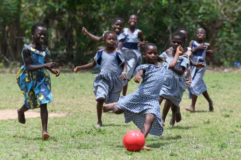 Girls in blue school uniforms play football in the grass.