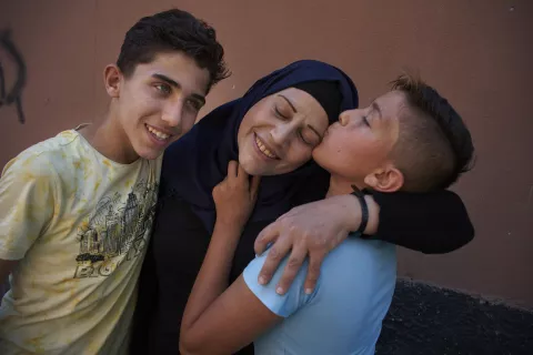 Two Syrian boys embrace and kiss their mother.