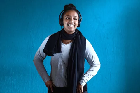 An adolescent girl wearing headphones and a long blue scarf smiling