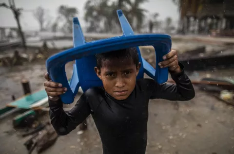 Nicaragua. A child protects himself from the heavy rain with a plastic chair.