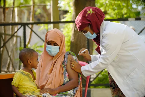 Munta Hussen gets her first COVID-19 vaccine as her son looks on.
