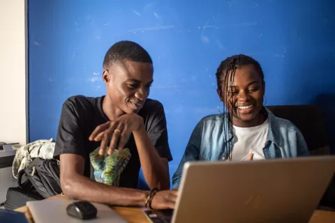 Two young digital volunteers sit at a desk looking at their laptop. 