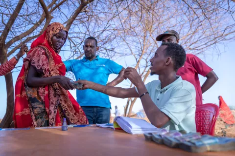 Ethiopia. A man sitting at a table hands a woman cash as part of a UNICEF-supported cash grant programme to help families improve their nutritional status.
