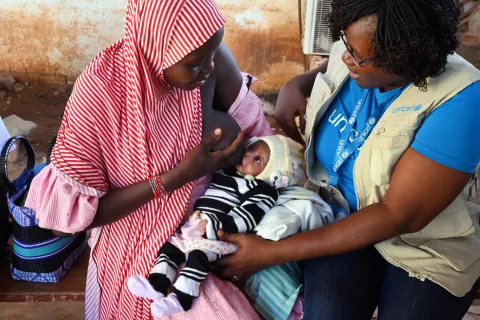 A mother holds her baby, who is being examined for malnutrition by a UNICEF staff.