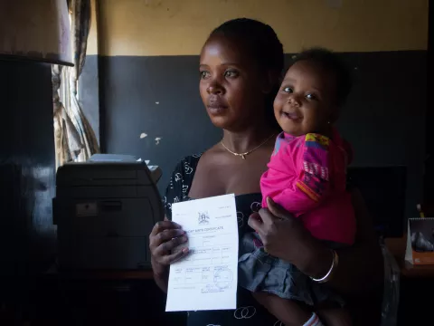 A mother displays her child's birth certificate while holding her child in a hospital in Uganda.