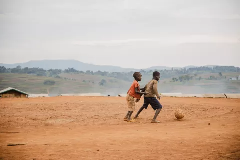 Two children play football in a desert field.