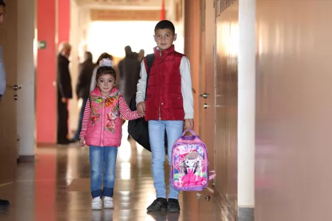 A boy and a girl stand in the hallway of a school holding their backpacks