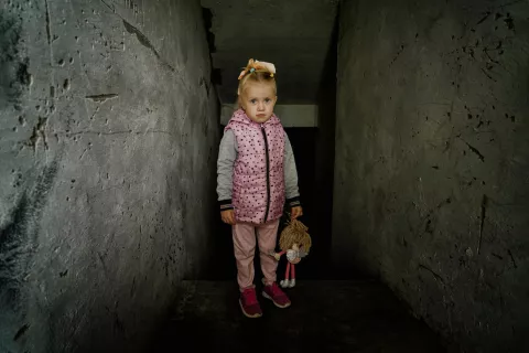 Ukraine. A young girl stands holding a toy in the boiler room of her school.
