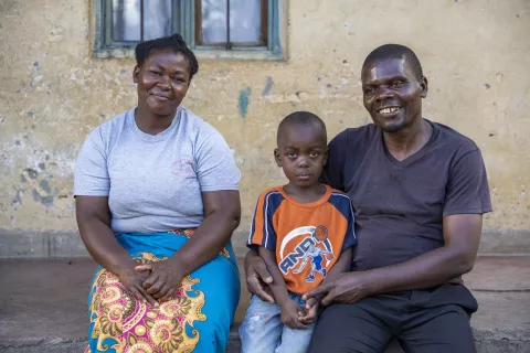 James Chinomba, a health worker, and his wife Eveness with their youngest son Wisdom sit on the porch of their house