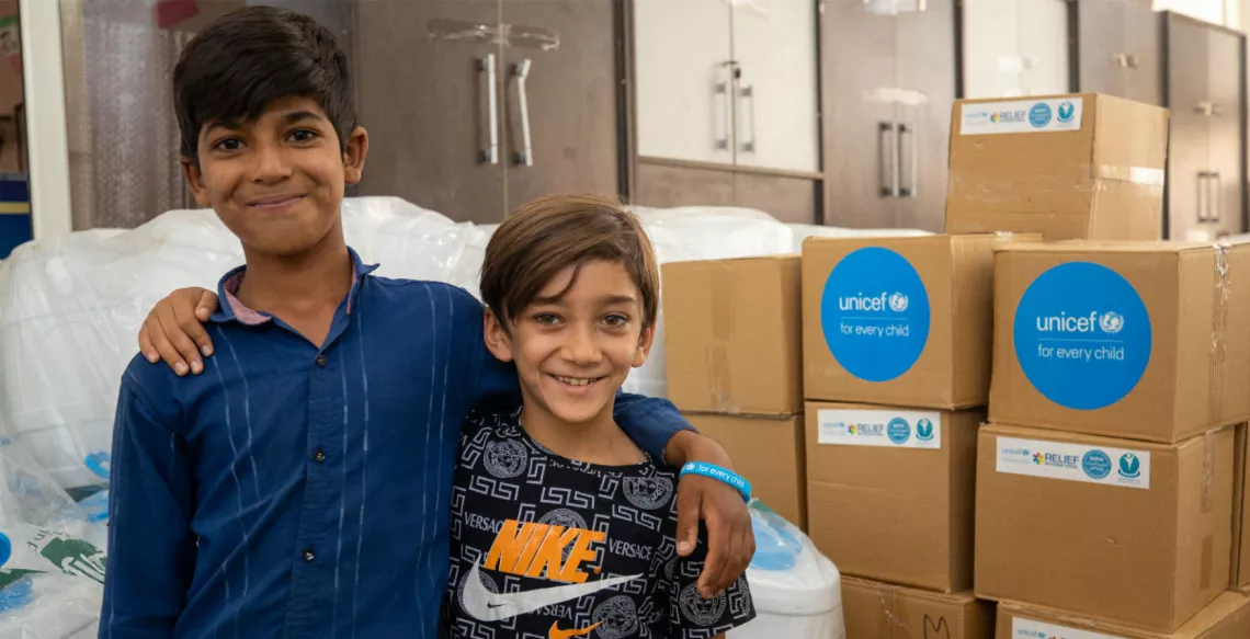 Two boys pose in front of boxes of supplies