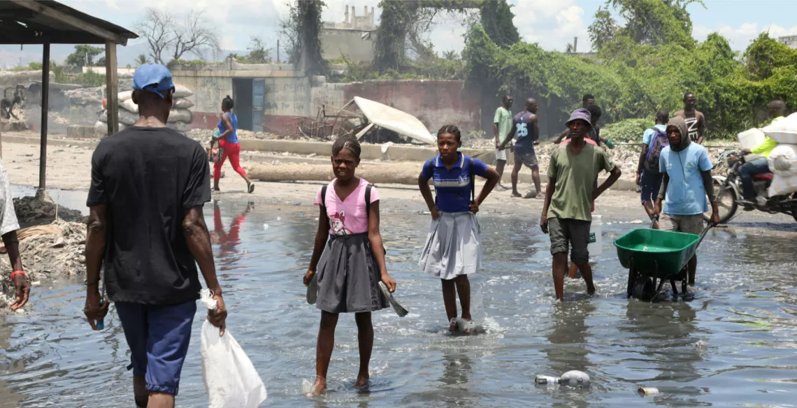 People cross a waste-filled waterway