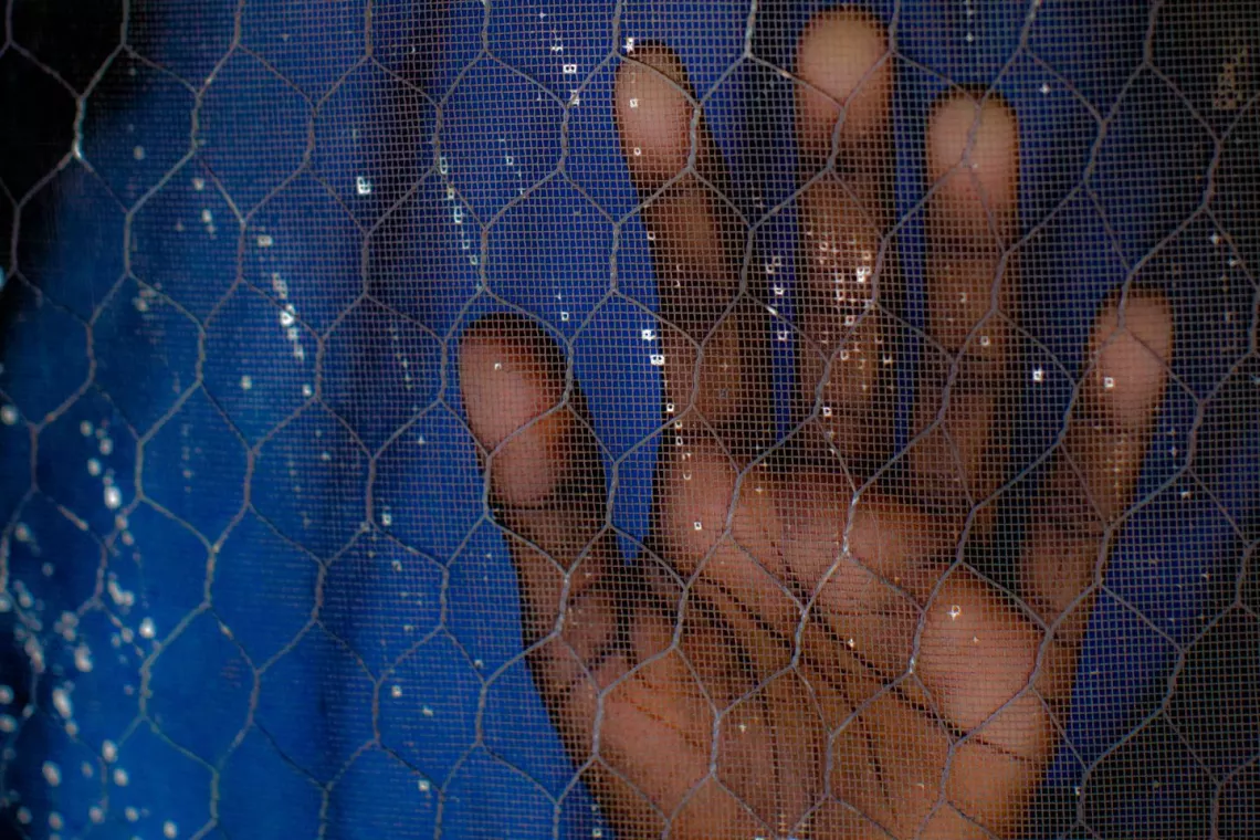 Nigeria. A girl holds her hand against the mesh of a door.