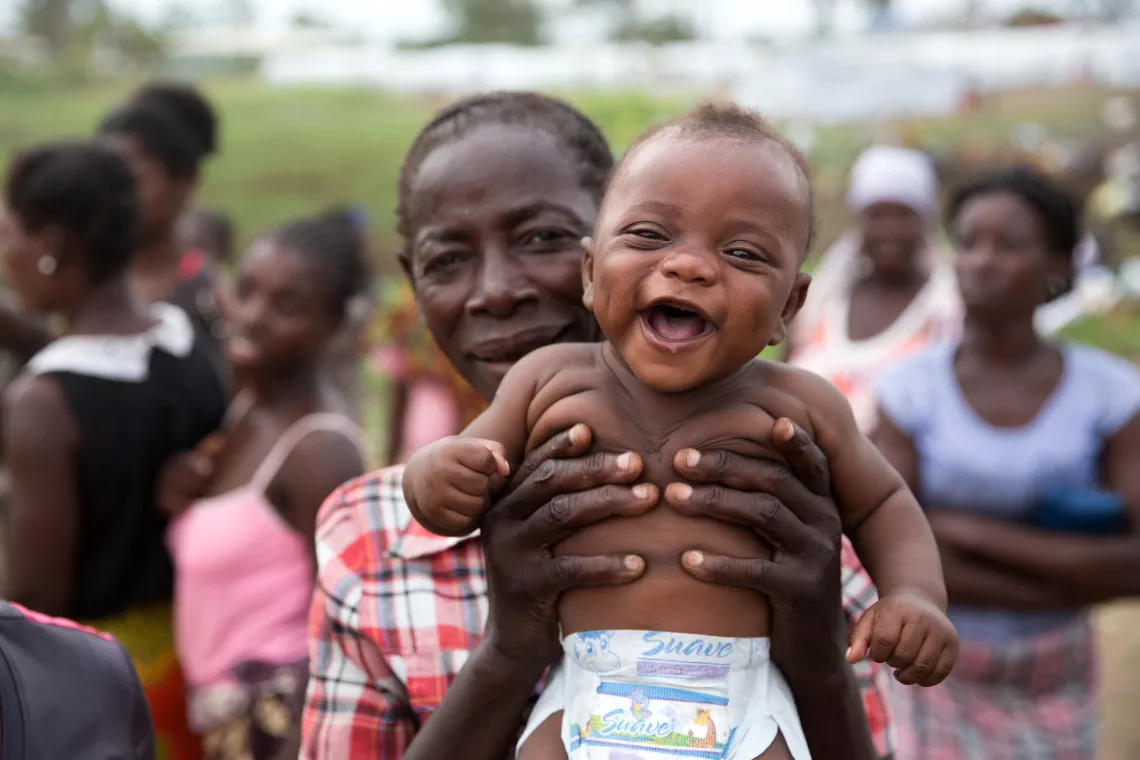 A woman holds a smiling baby in front of her.