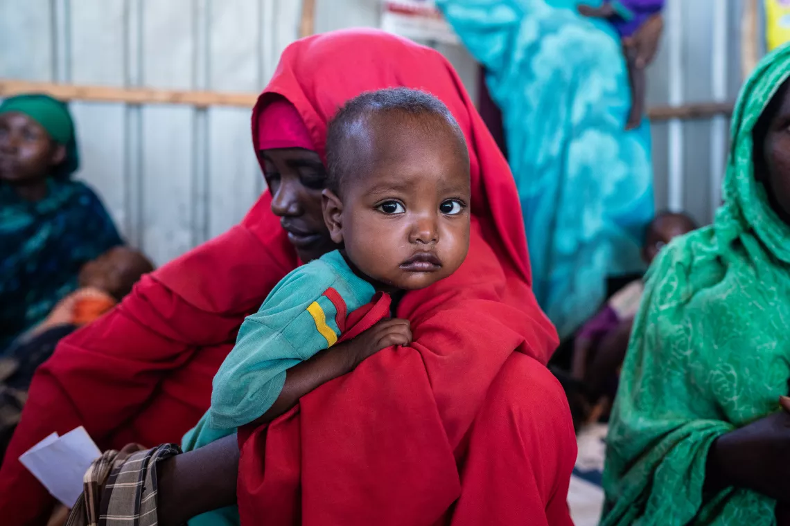 A woman in red holds her son over her shoulder in a health centre.