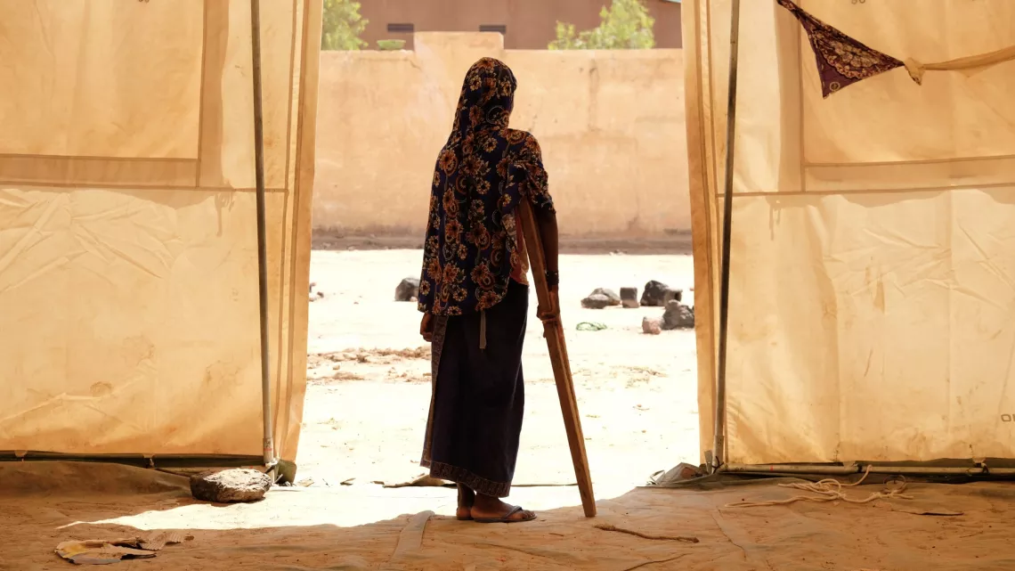 Mali. A displaced girl leans on a crutch outside a tent.