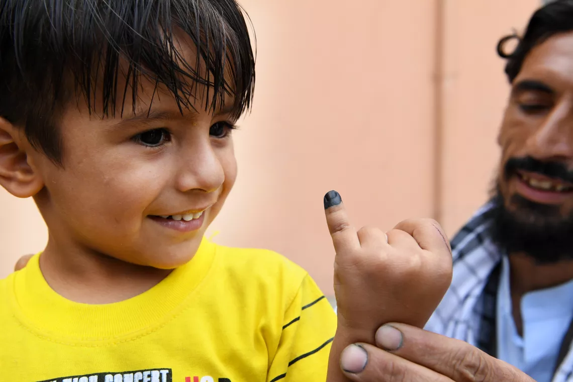 A boy raises a finger marked by a polio vaccinator, Afghanistan