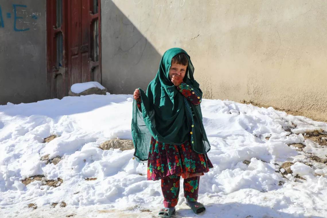 Afghanistan. A girl stands in front of her home using her hand to keep her nose warm.
