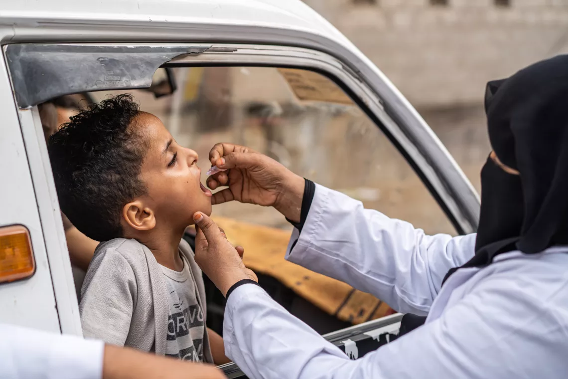 Una trabajadora de la salud vacuna a un niño de 5 años dentro de una camioneta, durante una campaña de inmunización contra la poliomielitis.