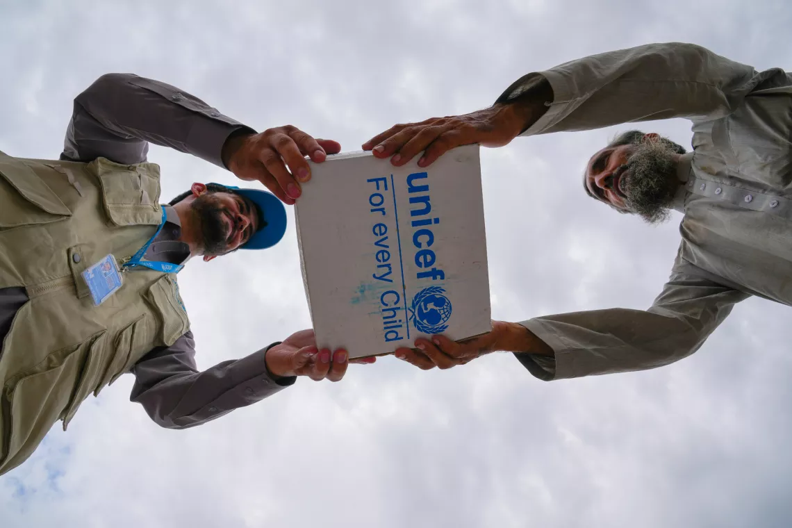 Two men holding a UNICEF supply box