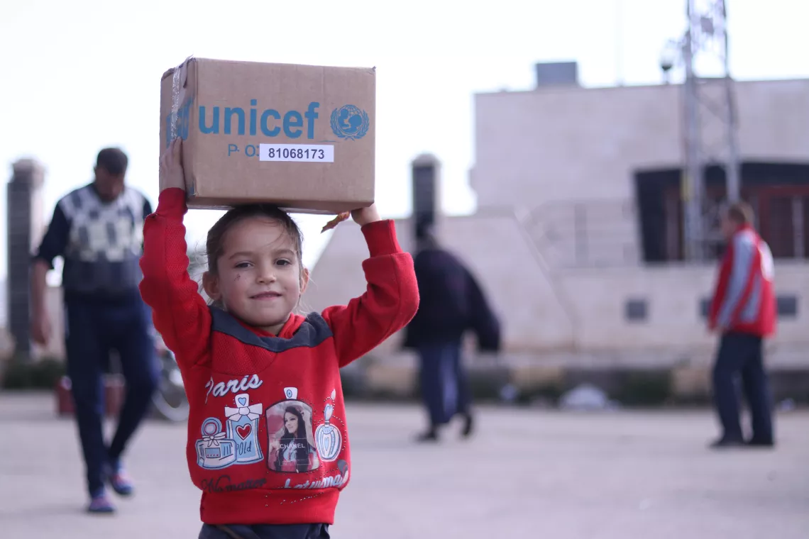 Syria. A child carries a box of UNICEF-supported winter supplies in rural Homs.