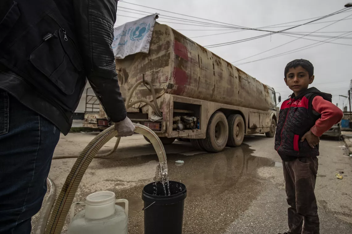 Un niño de pie junto a la manguera de suministro de un camión cisterna que abastece agua potable en Siria con ayuda de UNICEF. 