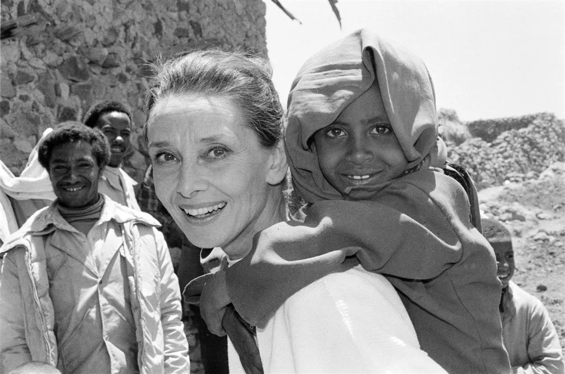 UNICEF Goodwill Ambassador Audrey Hepburn smiles as she carries a child on her back, in the northern town of Mehal Meda in Shoa Province, Ethiopia. Ms. Hepburn was visiting a food distribution centre in the town.