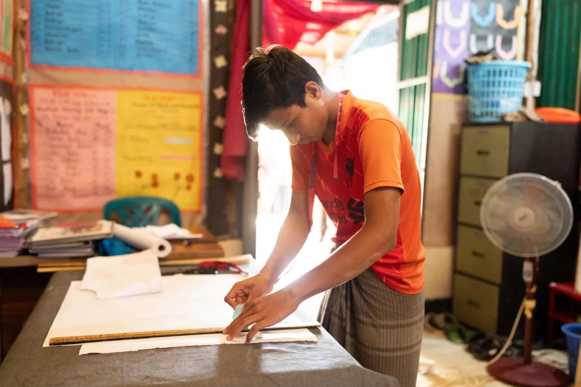 Bangladesh. Saiful Islam, 17, lines up a ruler on some paper at a tailoring workshop at a Multi-Purpose Centre in a Rohingya refugee camp in Cox’s Bazar.