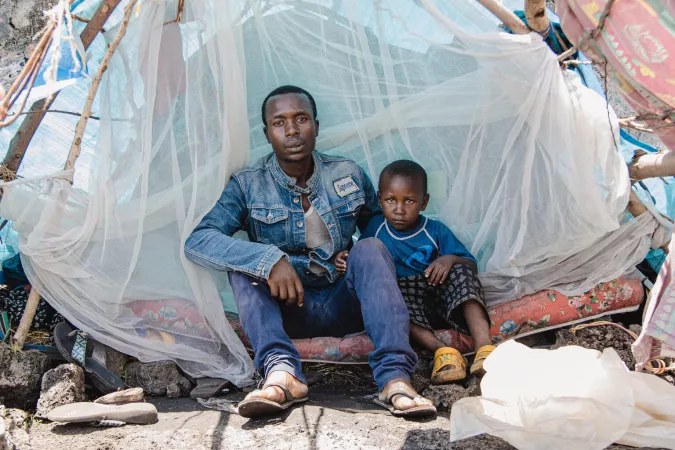 A man and son sit together inside a tent in a camp for displaced people.