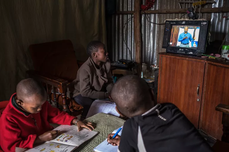 Elizabeth, 12 ans, et Justin, 10 ans, suivent un cours de sciences sociales sur la chaîne EDU TV tout en faisant leur révision à la maison à Kibera. Le frère de Justin, Morara, qui est à la maternelle, griffonne un cahier d'exercices. Elizabeth est en sixième année et Justin en cinquième année. "Je connais la plupart des sujets enseignés par le professeur", dit-il. 