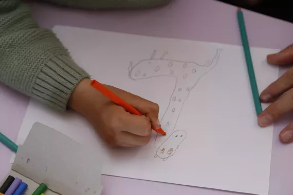 A child's hand drawing a giraffe on paper