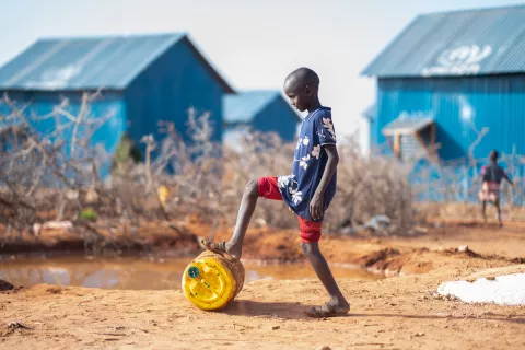 Young boy is rolling a water can to his home.